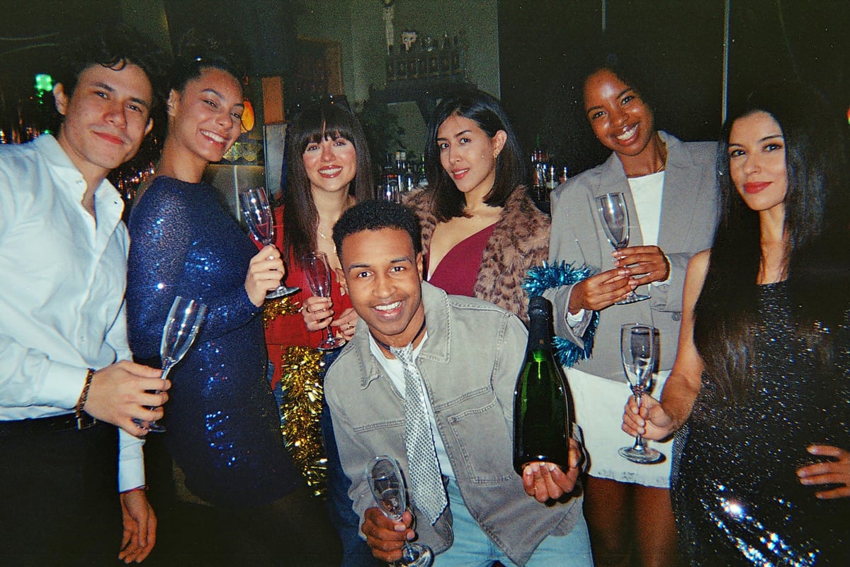 Diverse group of young adult friends smiling while holding champagne glasses and bottle, celebrating a special occasion with festive decorations