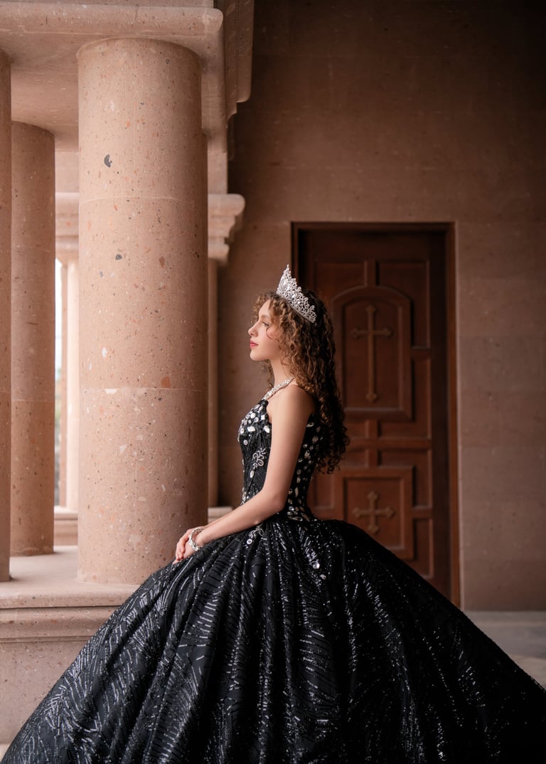 Woman in an elaborate black sequined ball gown with tiara standing beside a large stone column in a classical archway